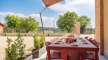 Un área de comedor al aire libre con una mesa preparada para seis personas, rodeada de sillas rojas, bajo un gran paraguas.