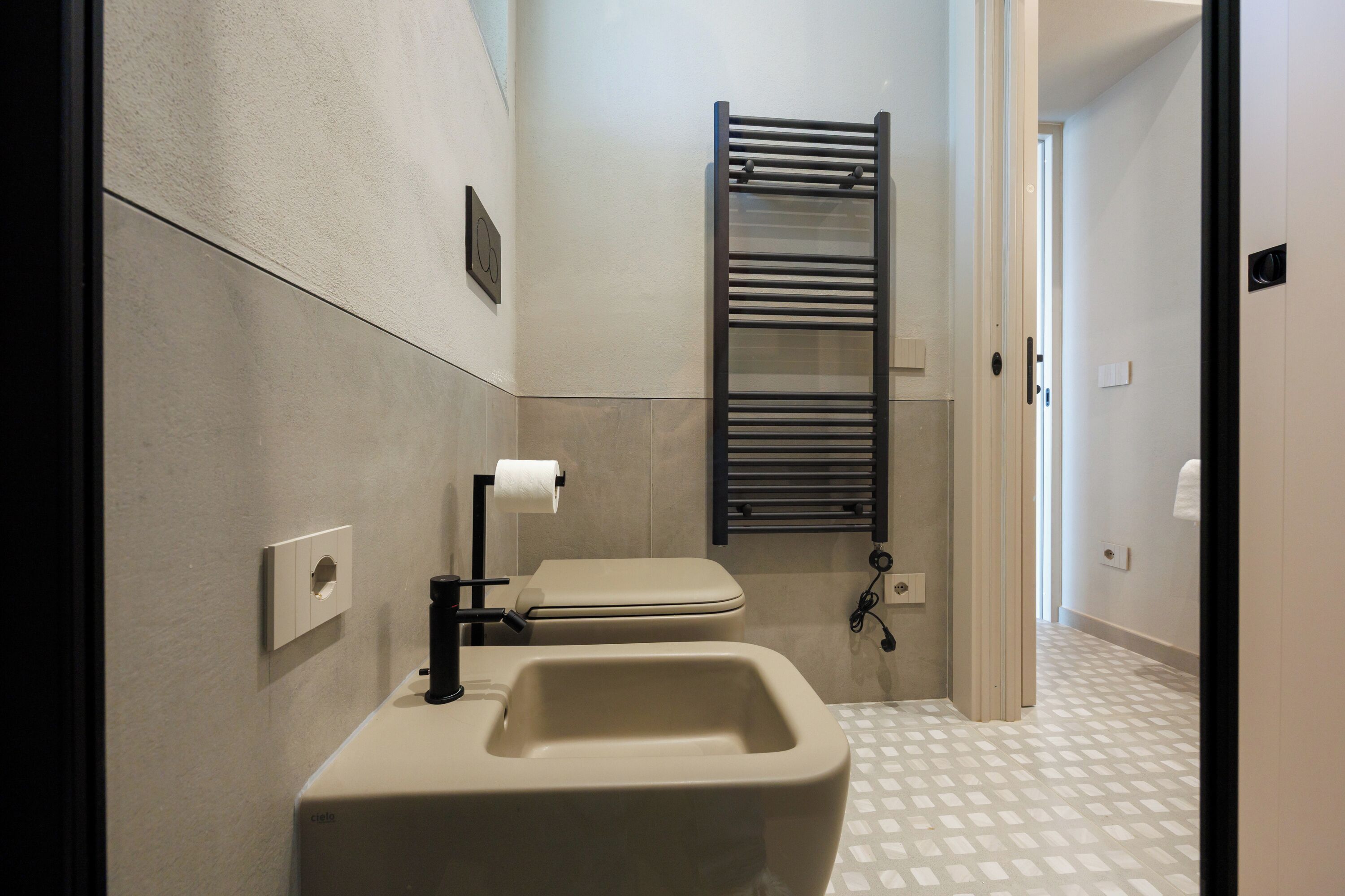 Een moderne badkamer met toilet, bidet, handdoekhouder en een vloer met patroon.