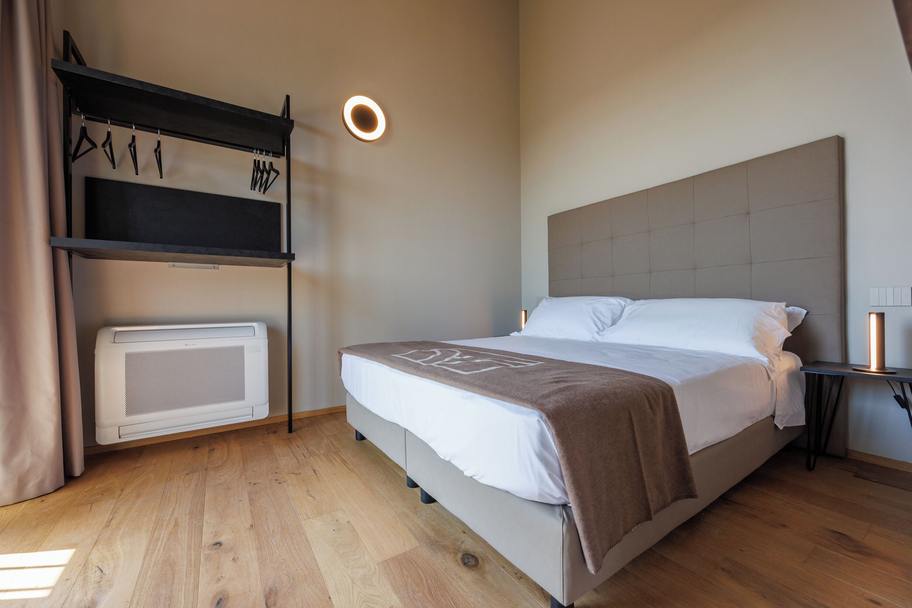 Un dormitorio con una cama, un calentador, un estante con perchas y una lámpara en el techo.