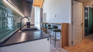 A modern kitchen with a black countertop, a stainless steel sink, and a wooden ceiling. There are bar stools and a door leading to another room. - Calanga (Barbaresco)