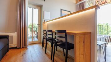 A compact living space with a kitchenette, a dining area with chairs, a sliding glass door leading to an outdoor balcony, and a bed with a view.
