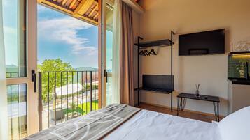 A bedroom with a bed, a TV, a shelf with wine glasses, and a view of a green landscape.