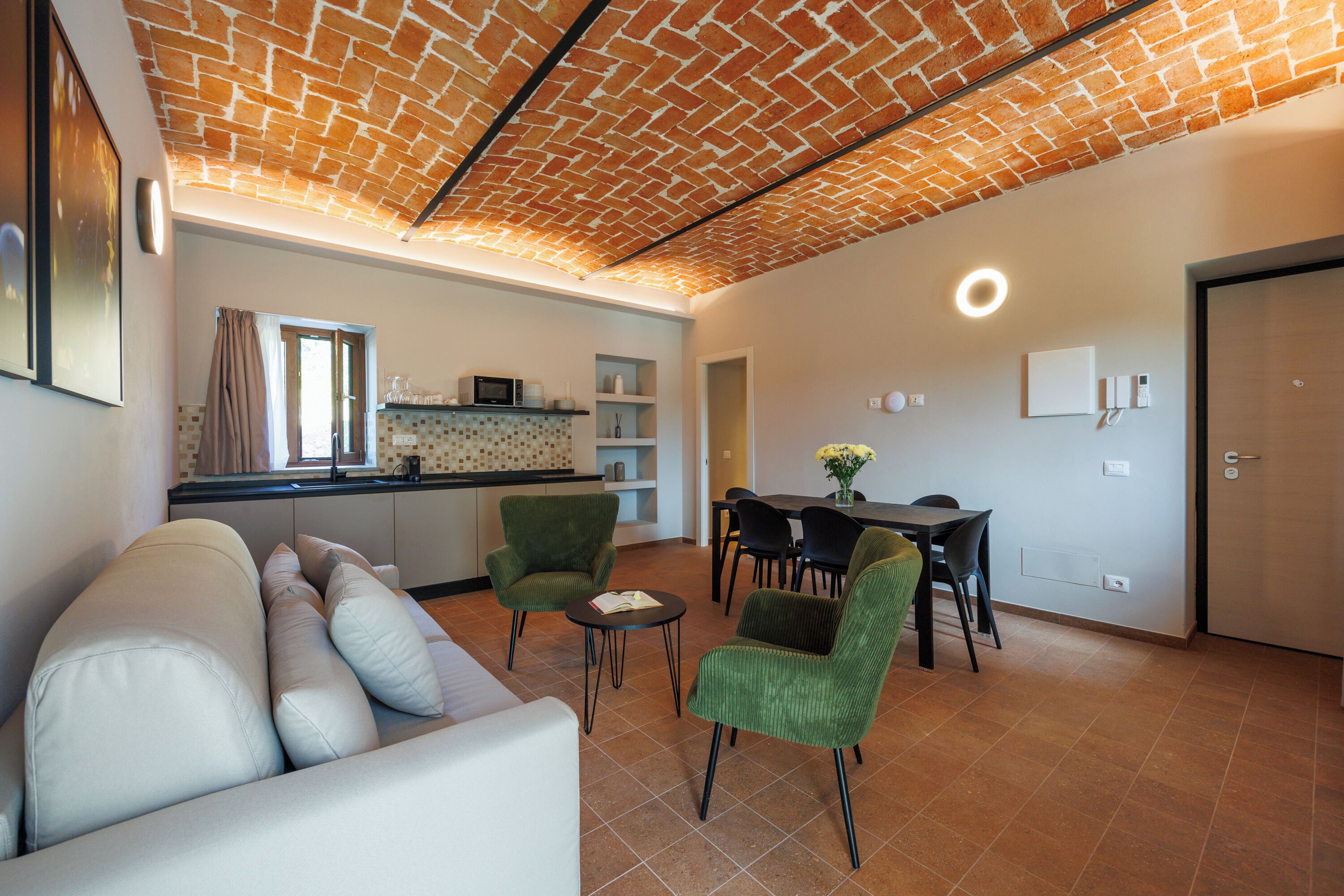 Una sala de estar moderna con sofá, sillas, una mesa de comedor y una cocina con techo de ladrillo.