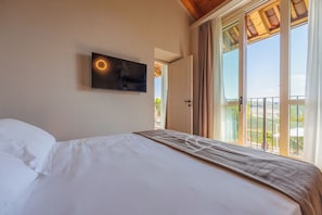 Une chambre d’hôtel avec un lit, un téléviseur fixé au mur et une grande fenêtre donnant sur l’extérieur.