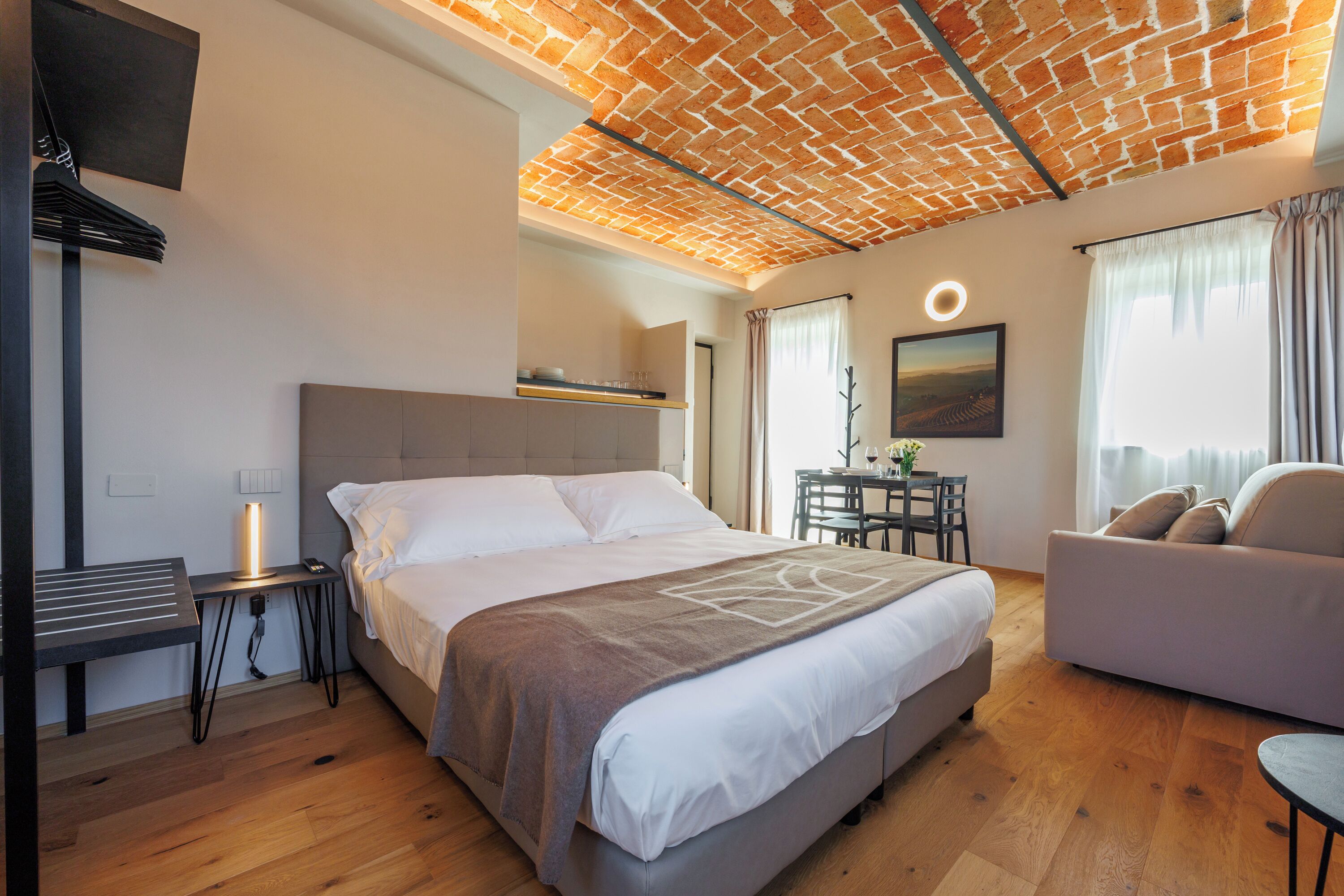 A modern hotel room with a large bed, a desk, a dining area, and a view of the countryside.