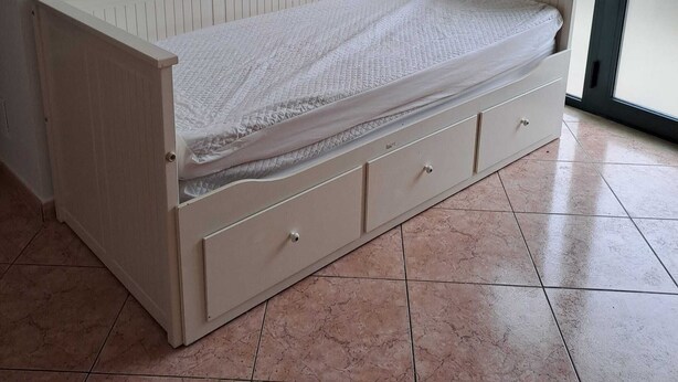 Een eenpersoonskamer met raam, radiator en tegelvloer.