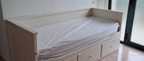Une chambre individuelle avec un lit simple, une fenêtre, un radiateur et un sol carrelé.