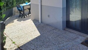 Een gebouw met een patio, een tafel met stoelen, een plant in pot en een deur met ruit.