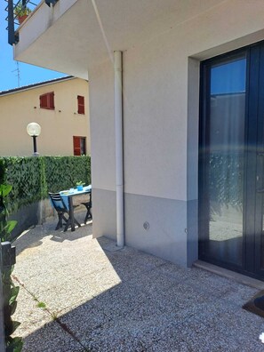 A building with a patio area, a table with chairs, a potted plant, and a door with a glass panel. - Casa Zefiro – Private Entrance with Courtyard, 10 min from the Beach (Marzocca)