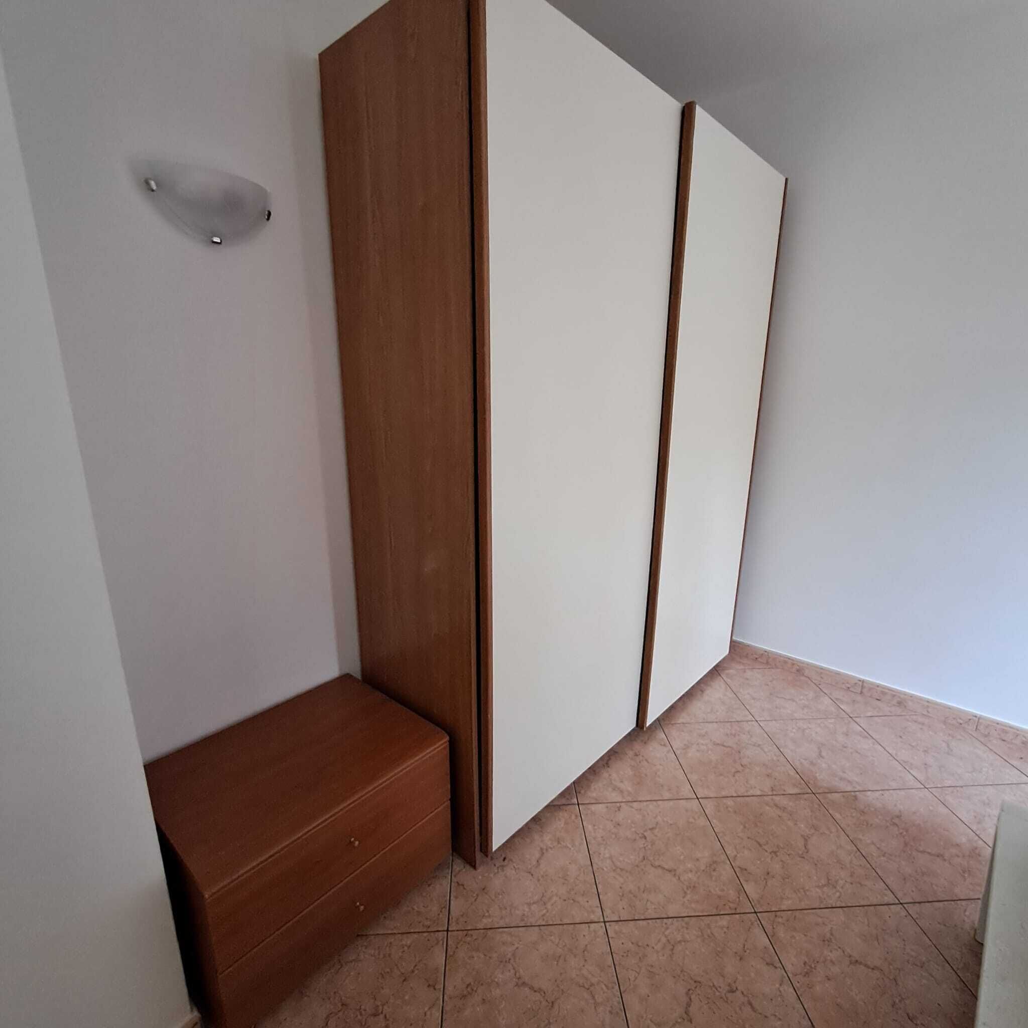 Une pièce avec un banc en bois, une armoire blanche et un sol carrelé.