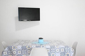 A dining area with a patterned tablecloth, a potted plant, and a mounted television on the wall. - Casa Zefiro – Private Entrance with Courtyard, 10 min from the Beach (Marzocca)