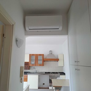 A compact kitchen with a built-in stove, a sink, and wooden cabinets. - Casa Zefiro – Private Entrance with Courtyard, 10 min from the Beach (Marzocca)