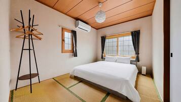 A hotel room with a bed, a hanging coat rack, a window with curtains, and an air conditioning unit.