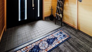 A modern interior with wooden paneling, a black door with illuminated panels, a shoe rack, and a patterned rug.