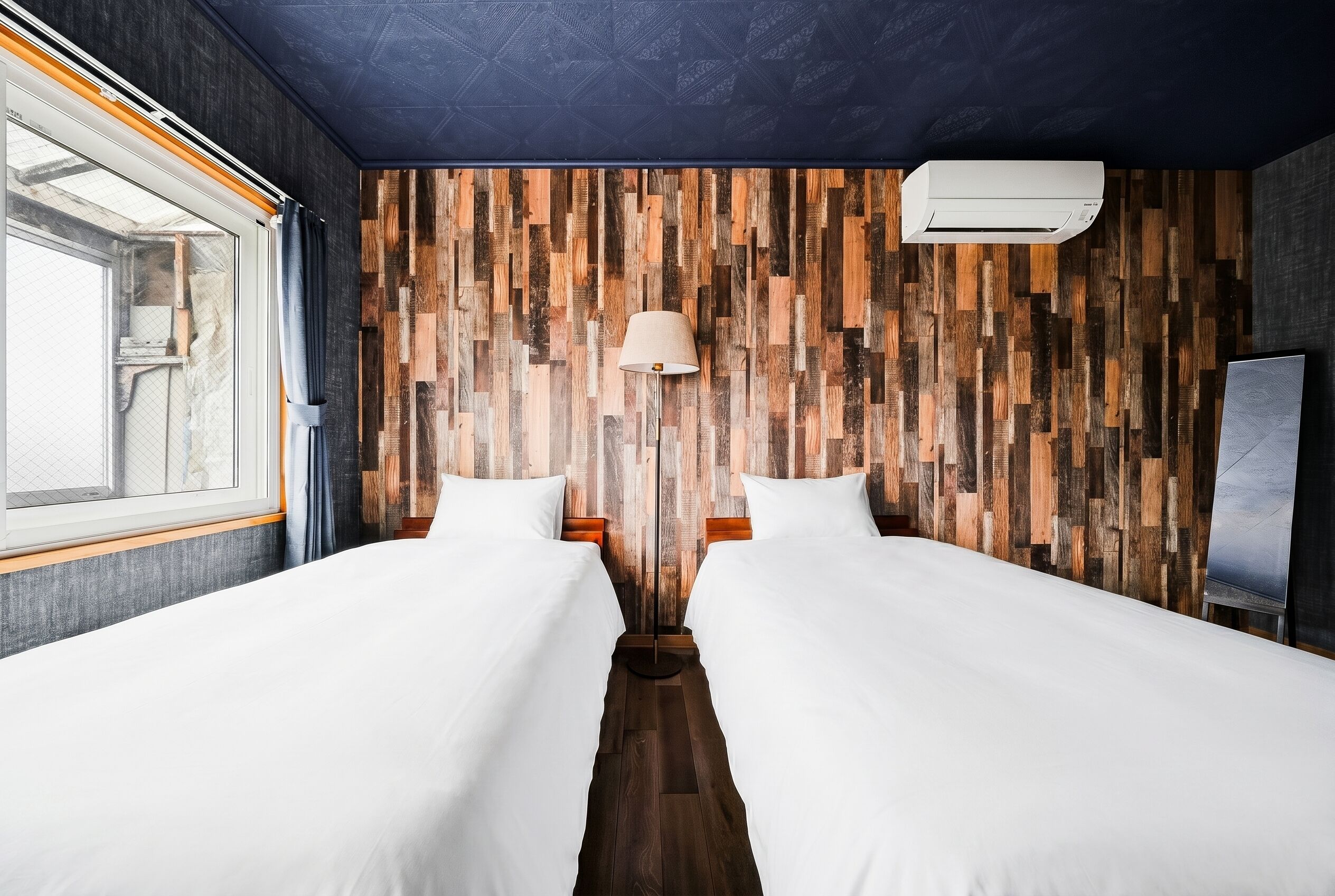 Une chambre d’hôtel avec deux lits, un panneau mural en bois, un luminaire au plafond et une fenêtre.