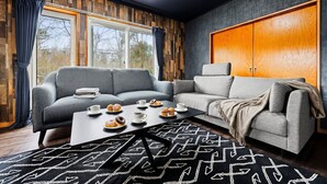A modern living room with a grey sofa, a coffee table with pastries, and a large wardrobe.