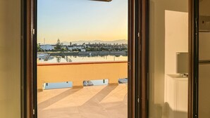Blick vom Balkon auf einen klaren Himmel, ein Gewässer und Gebäude in der Ferne.