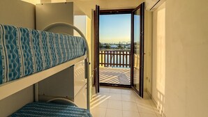 Ein Balkon mit Blick auf ein Gewässer und Gebäude, ein Stockbett mit gemusterten Betttextilien sowie eine Tür zum Balkon.
