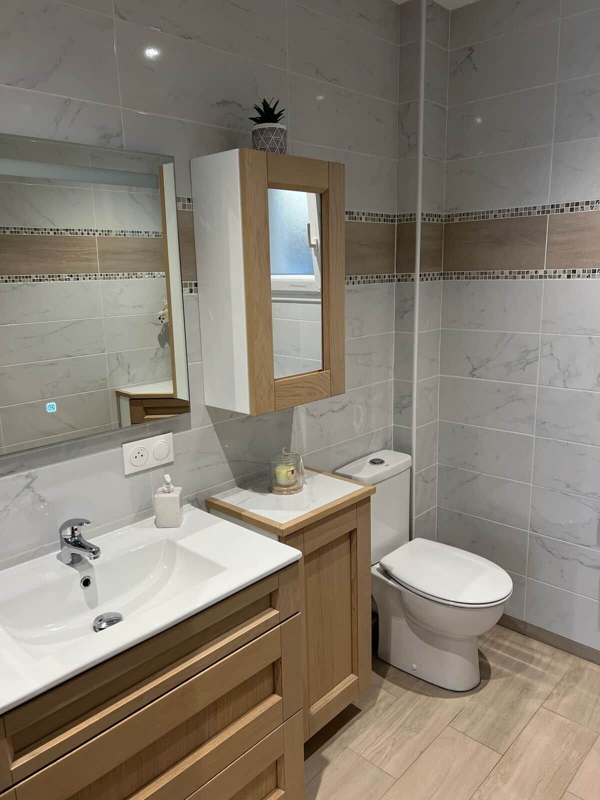 Un bagno con parete rivestita in marmo, un mobile contenitore in legno, uno specchio, un lavandino e un WC.