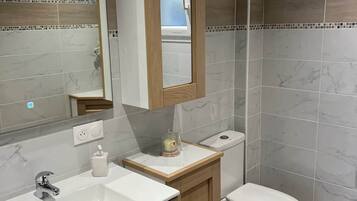 Un bagno con parete rivestita in marmo, un mobile contenitore in legno, uno specchio, un lavandino e un WC.