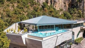 Un edificio moderno con piscina sul tetto, circondato dal verde e con montagne sullo sfondo.