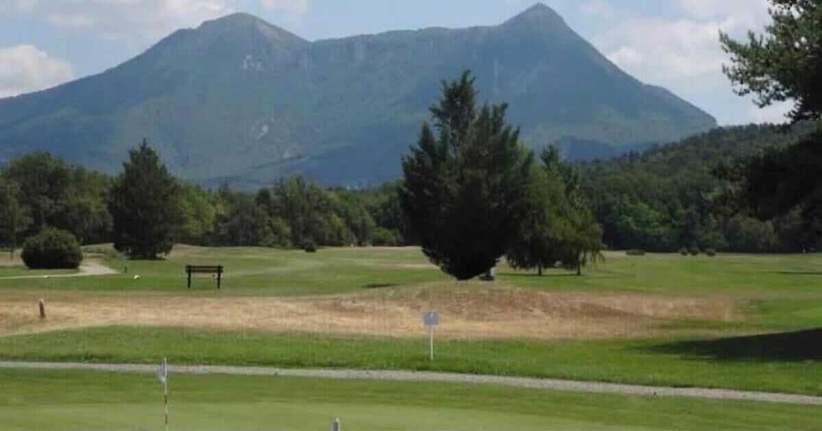 A golf course with a mountain in the background, a bench, and a signpost.