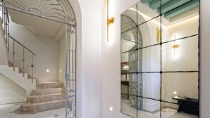 A staircase with a metal railing, a large mirror reflecting a staircase and a chandelier, and a wall-mounted light fixture. - Genteel Home Casa Pilatos Terrace (Seville)