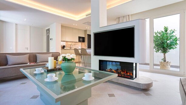 A modern living room with a glass coffee table, a sofa, a flat-screen TV, a fireplace, and a view of the kitchen. - Genteel Home Casa Pilatos Terrace (Seville)