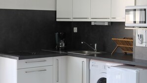 Et køkken med hvide skabe, en sort bordplade, kaffemaskine, vask, opvaskemaskine og mikrobølgeovn.