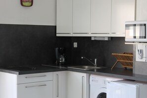 A kitchen with white cabinets, a black countertop, a coffee maker, a sink, a dishwasher, and a microwave. - STUDIO CABIN ON THE LEFT BANK (Palavas-les-Flots)