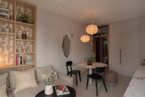 Ett modernt vardagsrum med en soffa, ett soffbord, ett matbord med stolar, en bokhylla och en hängande lampa.