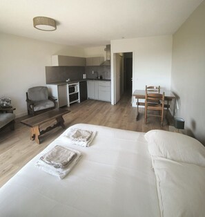 Une chambre d’hôtel moderne équipée d’un lit, d’une banquette, d’une chaise, d’une petite table, d’une kitchenette et d’un coin repas.