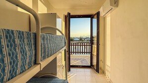 Ein schmaler Gang führt zu einem Balkon mit Blick auf Häuser und einem Zaun.
