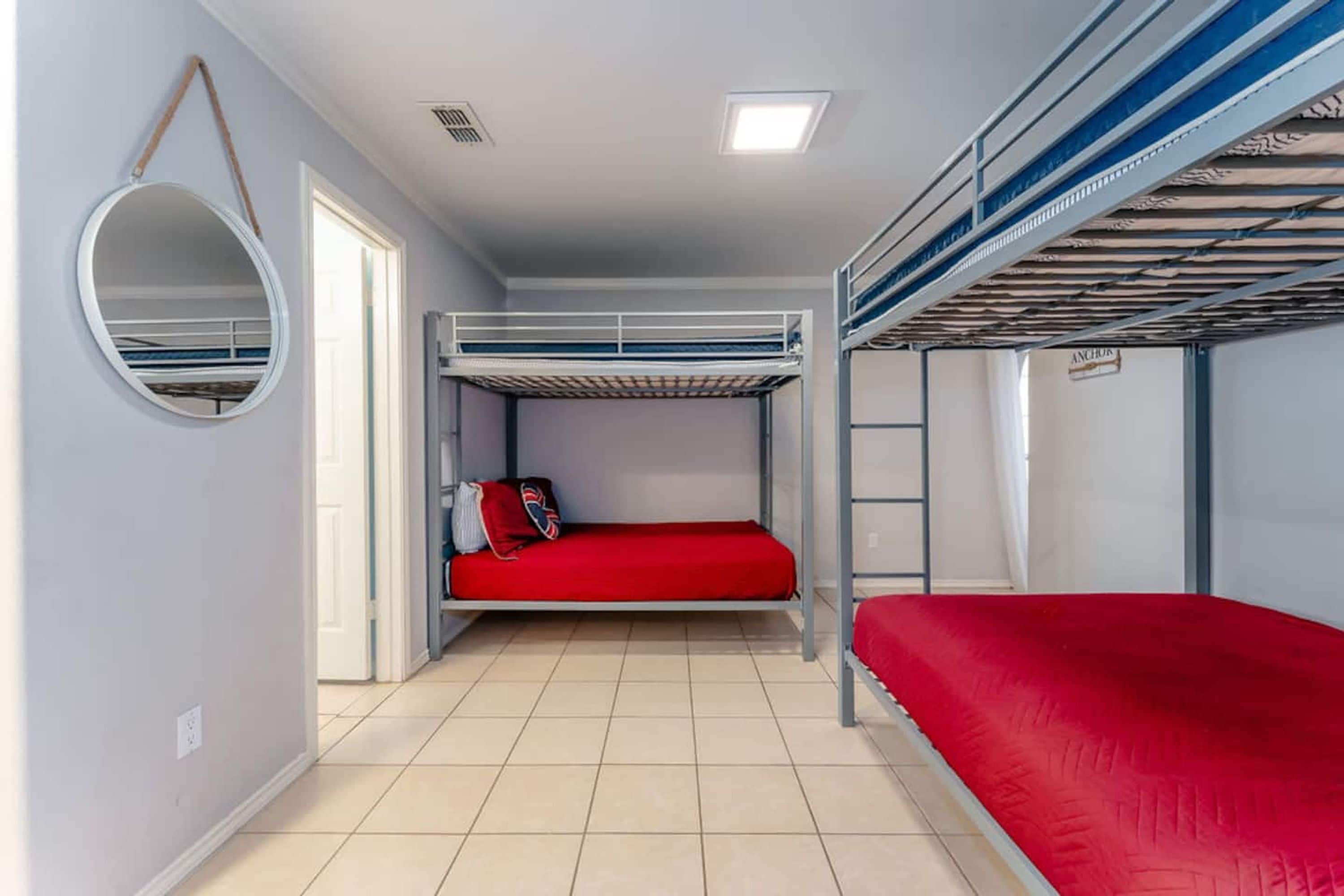 A bunk bed room with a red mattress, a round mirror, and a ladder.
