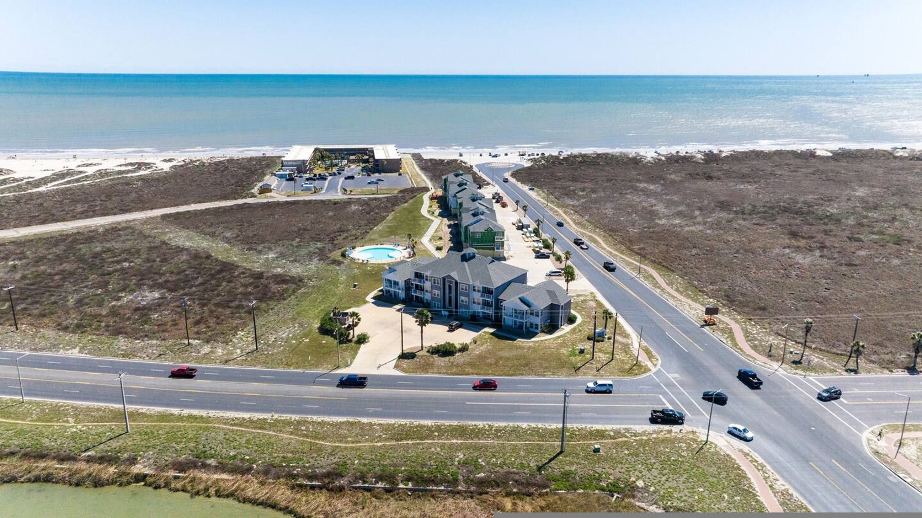 A coastal property with a large building, a swimming pool, and a road with vehicles.