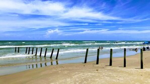 A beach with a clear sky, waves, and wooden posts. - Private Path to Whitecap Beach Pool 5 Stars (Corpus Christi)