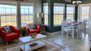 A living room with a dining area, large windows, a ceiling fan, and a sign on the wall. - Private Path to Whitecap Beach Pool 5 Stars (Corpus Christi)