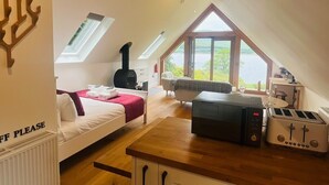 Een gezellige kamer met een bed, een tafel met een broodrooster, een open haard en uitzicht op de natuur.