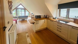 Een moderne keuken met een slaapkamer op entresol, houten vloeren en uitzicht op het landschap.