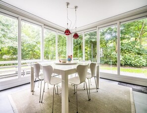 Ein moderner Essraum mit weißem Tisch und Stühlen, großen Fenstern und Blick ins Grüne.