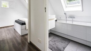 Un dormitori modern amb lliteres, un fanal i un bany amb banyera i plat de dutxa.