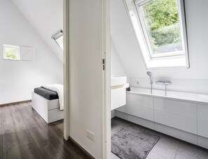 Ein modernes Schlafzimmer mit Schlafplatz in der Mansarde, einem Oberlicht und einem Badezimmer mit Badewanne und Dusche.