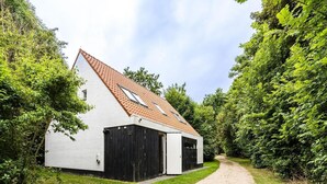 Un edifici blanc amb teulades vermelles, un camí de grava i vegetació densa.