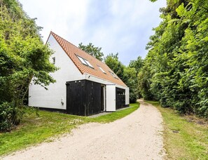 Ein weißes Gebäude mit rotem Ziegeldach, einem Kiesweg und dichter Bepflanzung.