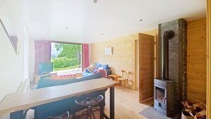 A modern living room with a sofa, a dining table, and a built-in wood stove. - Mésanges Chalet MSG NATURE & QUIET (10 people) (Châtel)