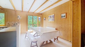A wooden-paneled room with a large table, benches, a kitchen area, and a view through a window. - Mésanges Chalet MSG NATURE & QUIET (10 people) (Châtel)