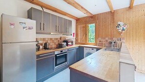 A modern kitchen with grey cabinets, a wooden countertop, a built-in oven, and a window with a view of greenery. - Mésanges Chalet MSG NATURE & QUIET (10 people) (Châtel)
