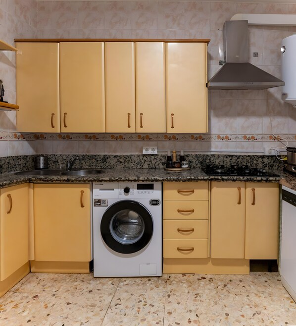 A kitchen with beige cabinets, a washing machine, granite countertops, and a stainless steel range hood.