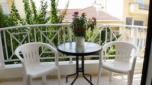 Un balcon avec deux chaises en plastique blanc, une petite table ronde et un pot de fleurs.