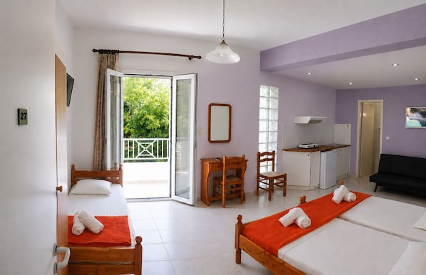 A hotel room with a bed, a desk, a chair, a sofa, and a balcony with a view of greenery.